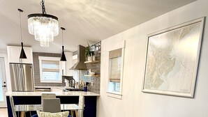 A modern living room with a blue sofa, a glass coffee table, and a chandelier. - Charming Southern Cottage (Savannah)