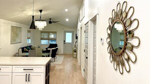 A spacious hallway with a chandelier, a decorative mirror, and a view of the living area with a couch and a dining table. - Charming Southern Cottage (Savannah)
