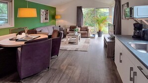 Een moderne woonkamer met een bank, een salontafel en een eethoek met een tafel en stoelen. Er is ook een keuken met een spoelbak en kasten.