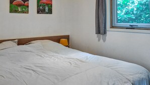 Een net opgemaakt bed met witte lakens, een houten hoofdbord, een bedlampje en twee ingelijste afbeeldingen van paddenstoelen aan de muur.