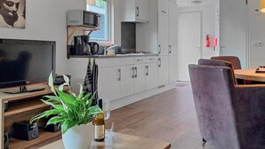 Een moderne keuken met witte kasten, een magnetron en een koffiezetapparaat. Er is een eethoek met een paarse stoel en een tafel.