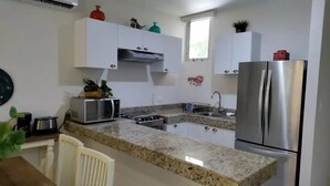 A modern kitchen with white cabinets, a granite countertop, stainless steel appliances, and a window above the sink. - Cozy 2BR Apt, 50 meters from the beach with large pool (Progreso)