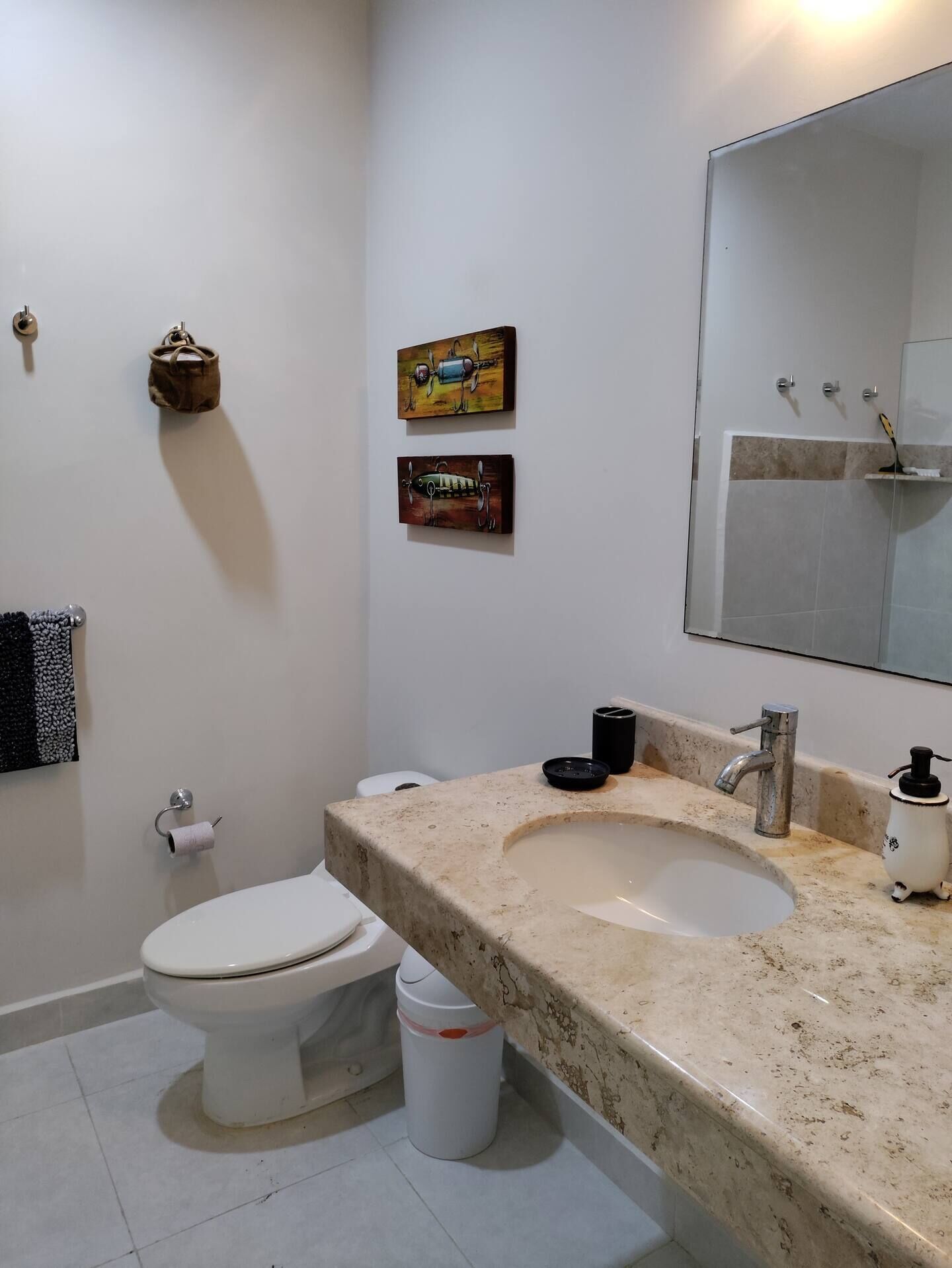Casa de banho com sanita, lavatório e duas pinturas penduradas na parede.