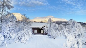 Ein mit Schnee bedecktes Blockhaus vor einer Bergkulisse.