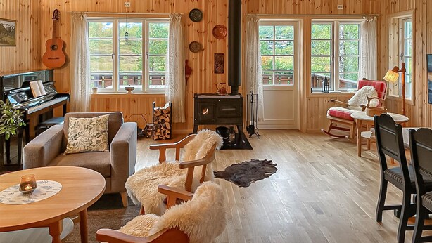 Ein gemütliches Blockhaus-Interieur mit Klavier, Gitarre, Kamin und Essbereich mit Holzmöbeln.