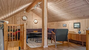 Ein gemütliches Holzhaus-Interieur mit Schlafkoje, Essbereich und einer Couch.