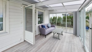 A conservatory with a grey sofa, a small table, and a wooden deck.