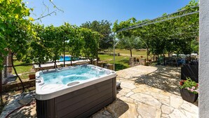 A hot tub in a backyard with a stone patio, a pool, and lush greenery. - Gorgeous home in Donji Kasic (Donji Kasic)