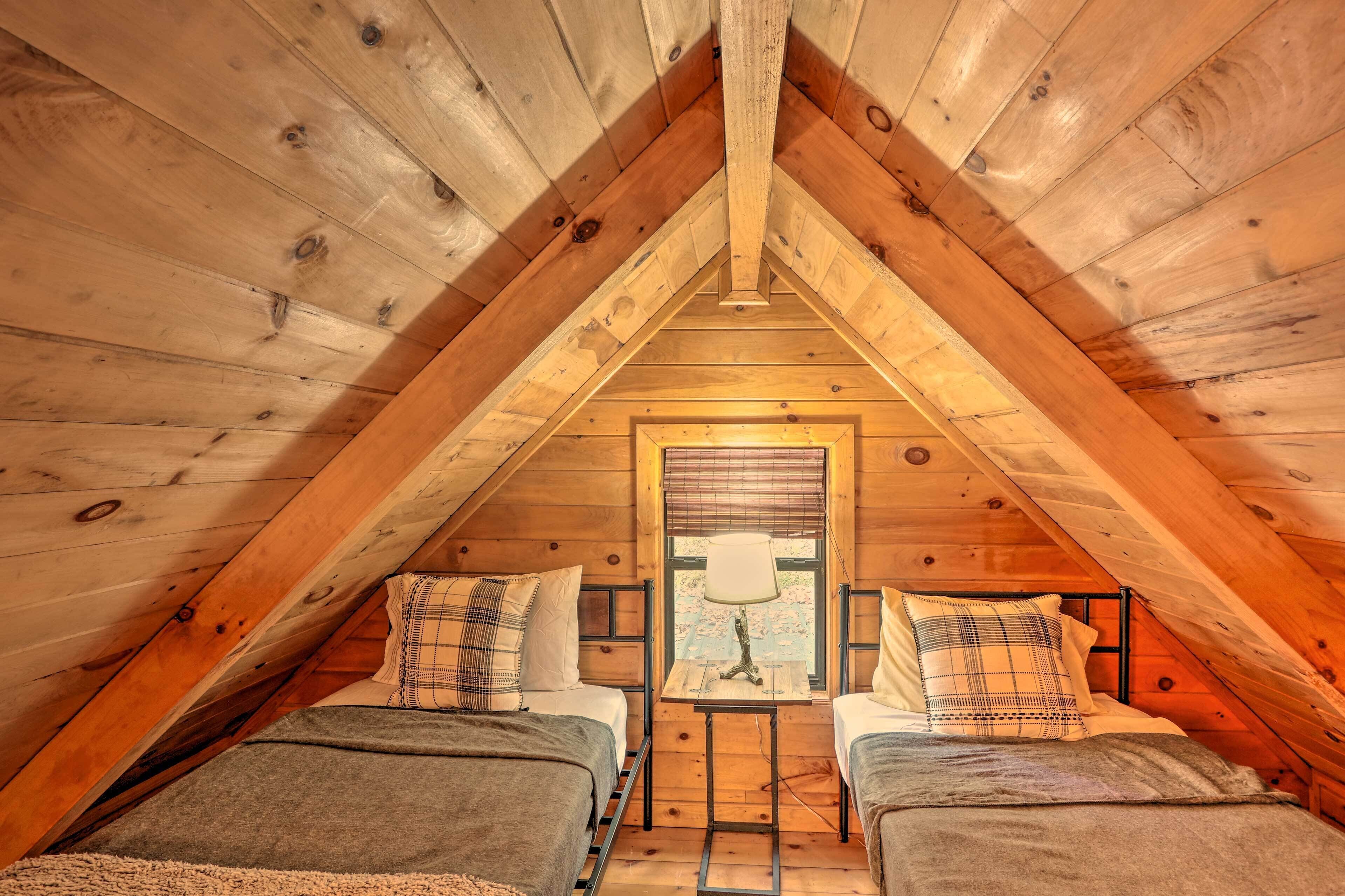 Une chambre confortable située sous les toits, avec deux lits, une petite table avec une lampe et une fenêtre équipée de stores.