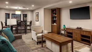 Un salon comprenant un canapé, un fauteuil, une table basse en bois, un téléviseur, une bibliothèque et un coin repas avec des chaises et une table.