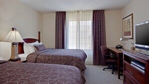Een hotelkamer met twee bedden, een bureau, een stoel, een televisie en een lamp.