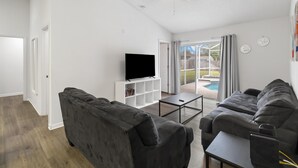 A modern living room with a flat-screen TV, two sofas, a coffee table, and a ceiling fan. - Amazing 4/3 house with private pool, near Disney! (Davenport)