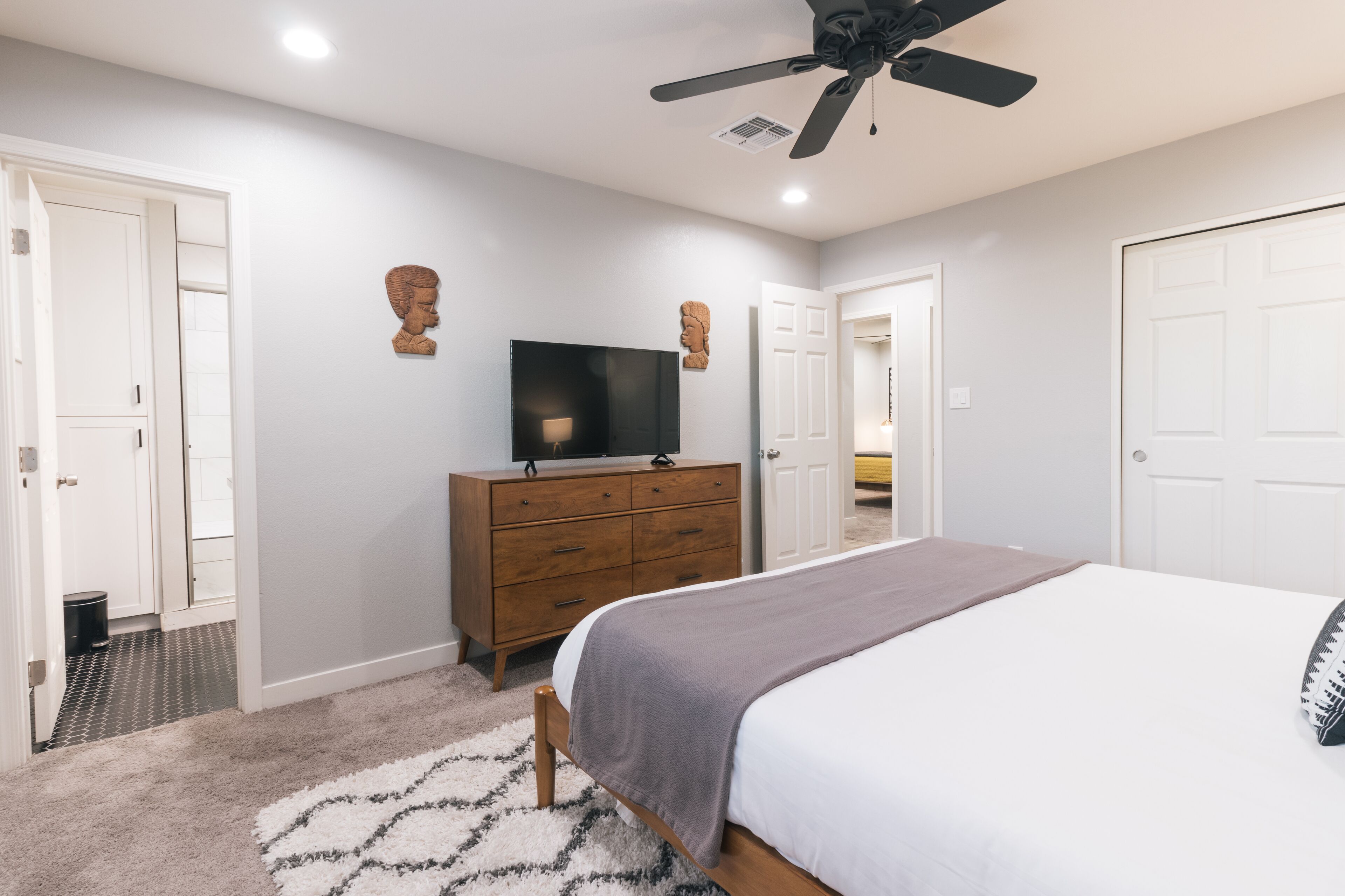 A bedroom with a bed, a dresser, a ceiling fan, and a TV.