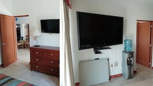 Habitación de hotel con televisión de pantalla plana, dispensador de agua, refrigerador y cómoda de madera.