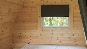 A small, wooden cabin room with a single bed, a window with a blind, and a view of trees outside. - Lavender is a cosy pod on the site of the Centry Touring Park in Brixham. (Brixham)