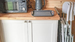 A kitchenette with a microwave, a kettle, and a grater on a wooden countertop. - Lavender is a cosy pod on the site of the Centry Touring Park in Brixham. (Brixham)