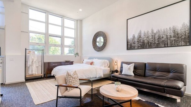 Une chambre à coucher moderne avec un grand lit, un canapé en cuir, un miroir rond et un tableau représentant une forêt.