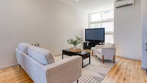 Un salon moderne avec un canapé, un fauteuil, un téléviseur et une petite table sur laquelle est posée une plante.