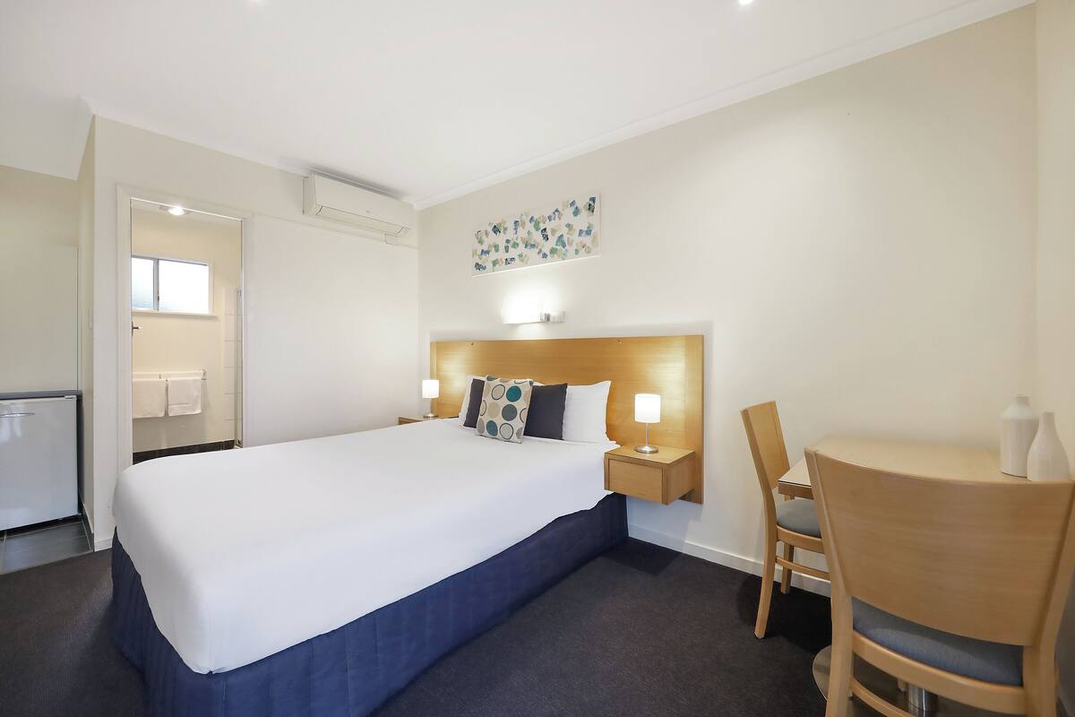 A hotel room with a large bed, bedside tables with lamps, a wooden chair, and a small table.