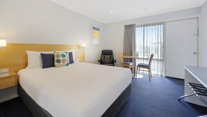 Quarto de hotel com uma cama grande, uma escrivaninha, uma cadeira e uma janela com cortinas.
