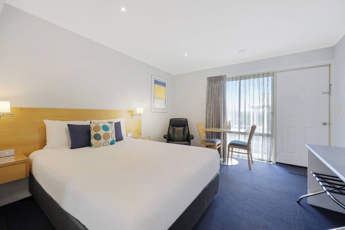 A hotel room with a large bed, a desk, a chair, and a window with curtains.