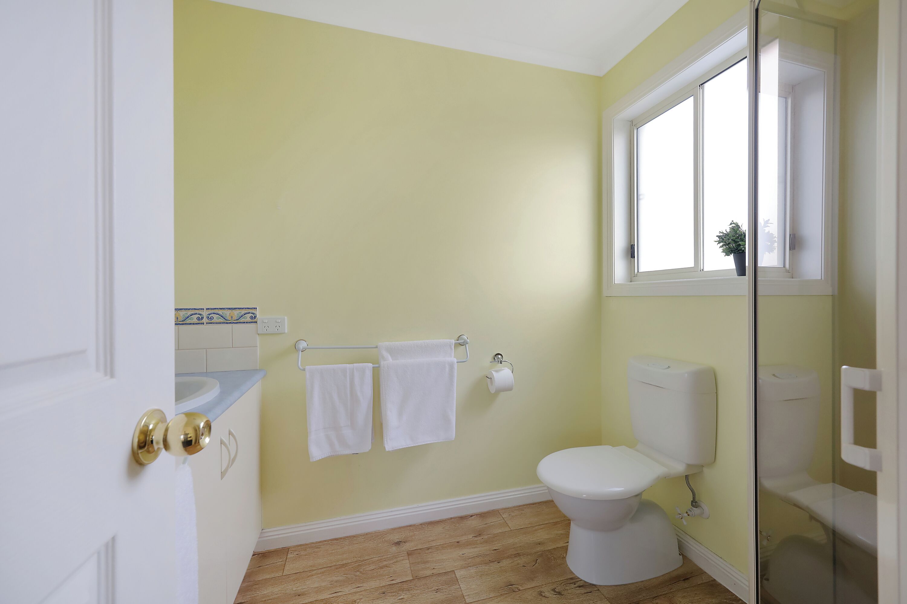 A bathroom with a toilet, a sink, and a shower. There are two towels hanging on a rack.