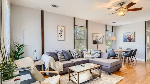 A modern living room with a sectional sofa, a coffee table, and a dining area with chairs. - 717 Woodward · Historic Southern Belle - Walk to Hot Spots! (Atlanta)