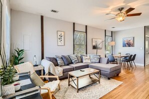 A modern living room with a sectional sofa, a coffee table, and a dining area with chairs. - 717 Woodward · Historic Southern Belle - Walk to Hot Spots! (Atlanta)