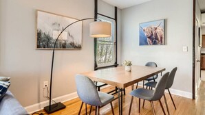 A modern dining area with a wooden table and grey upholstered chairs, a floor lamp, and two framed artworks on the walls. - 717 Woodward · Historic Southern Belle - Walk to Hot Spots! (Atlanta)
