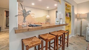 Una cucina con piano in legno, sgabelli da bar, un murale e un mobiletto giallo.