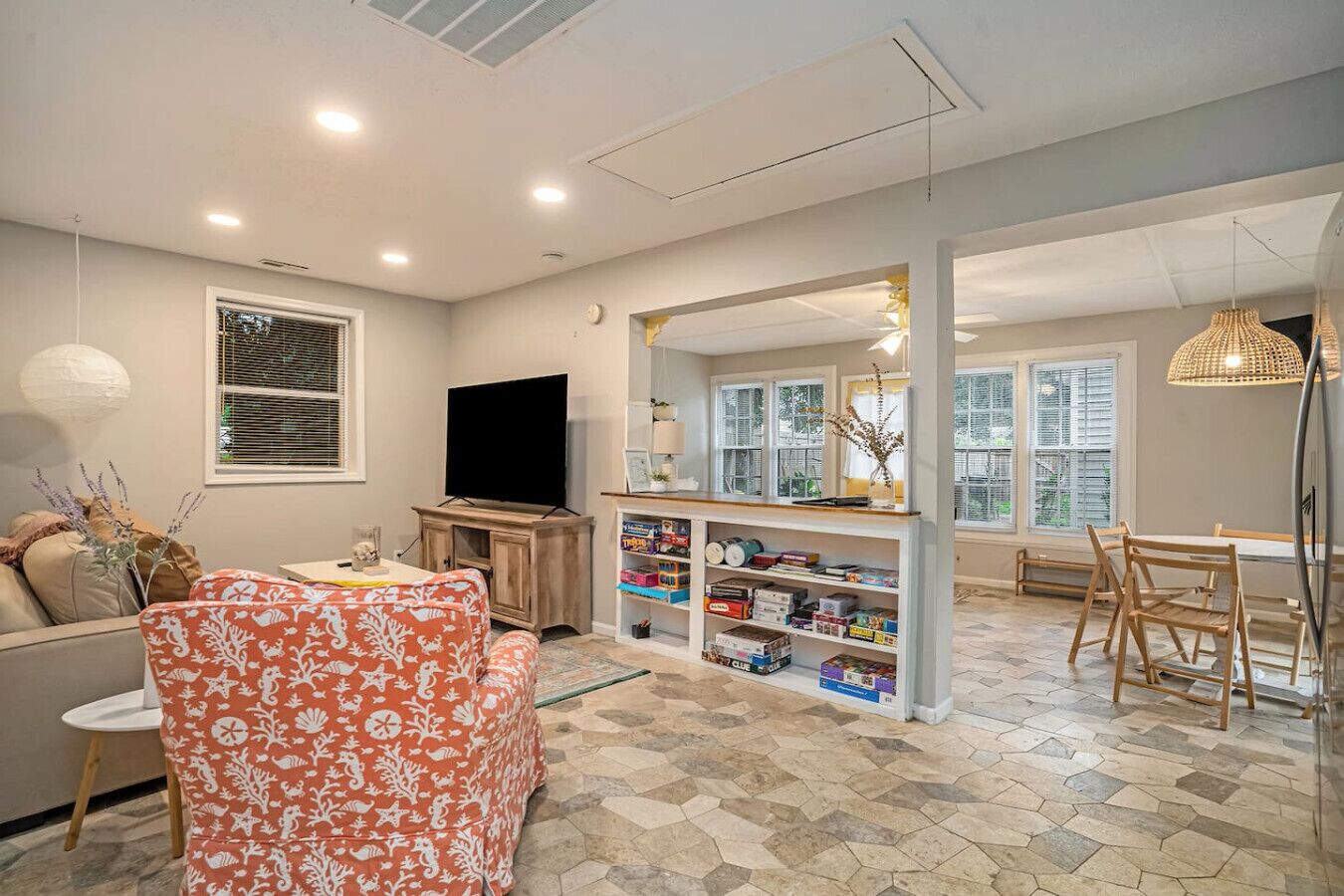 Een woonkamer met een bank, een televisie, een boekenkast en een eethoek met stoelen.