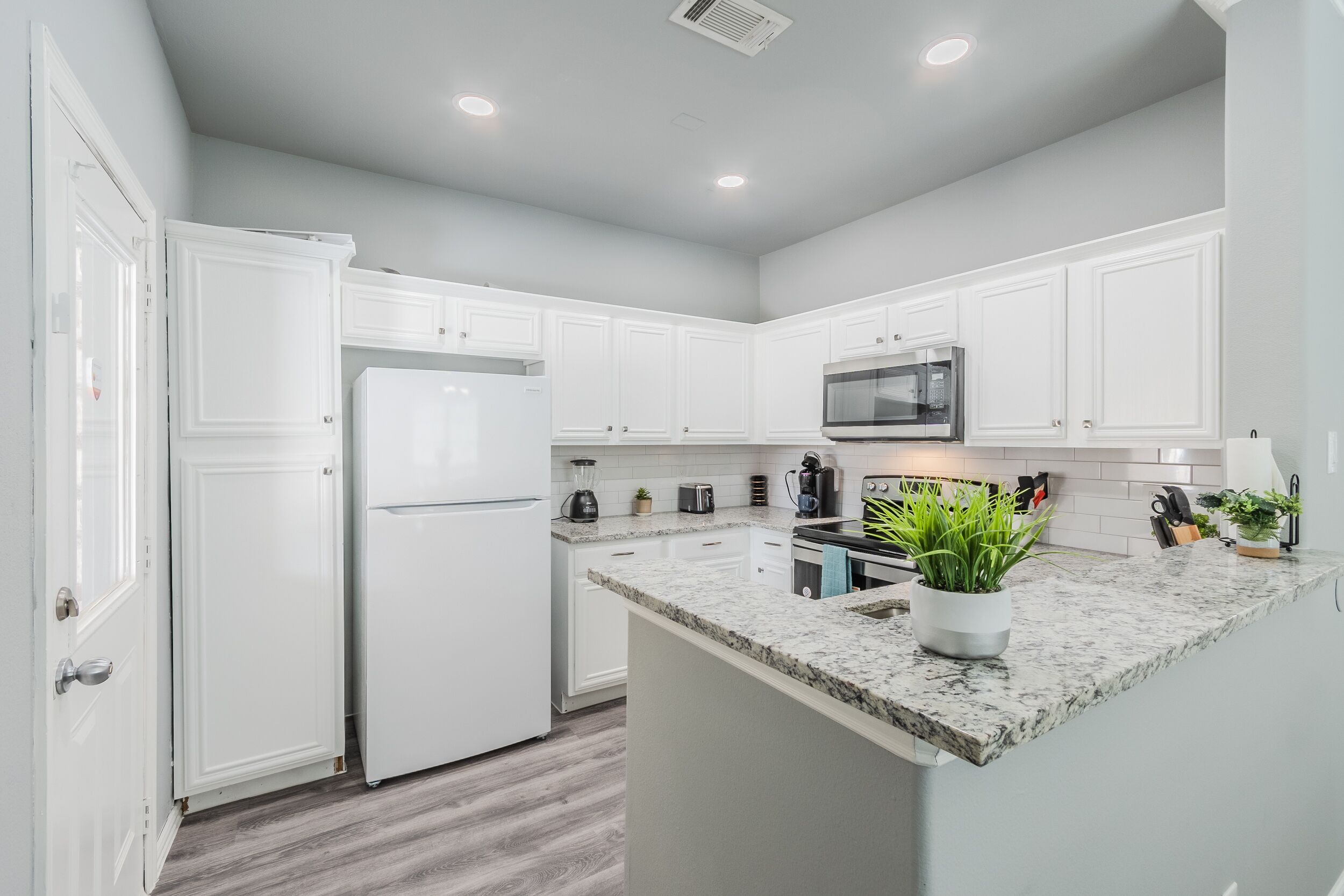 A modern kitchen with white cabinets, a granite countertop, and a built-in microwave.