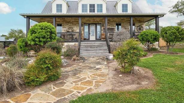 Une maison à deux étages avec une façade en pierre, un porche couvert et un chemin en pierre menant à l’entrée.