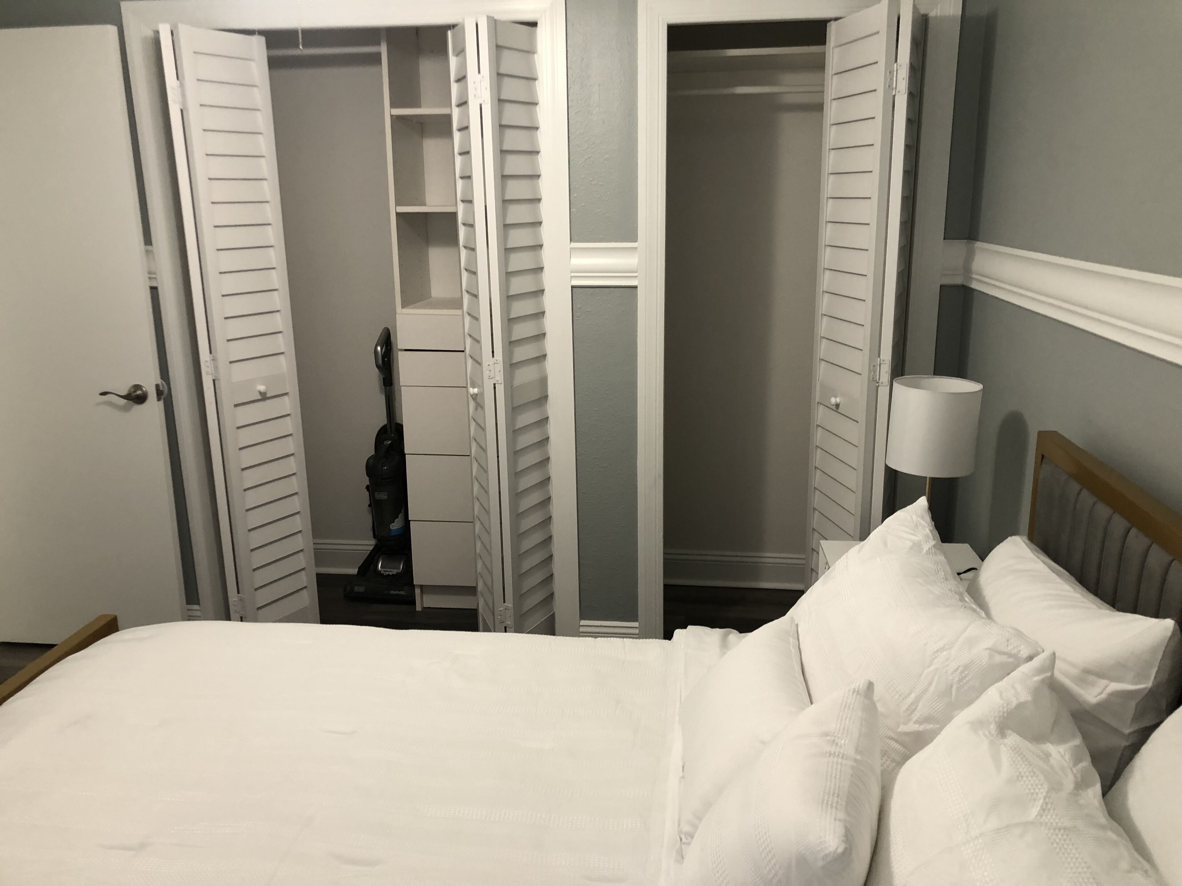 Ein Schlafzimmer mit einem Bett, weißen Kissen, einem Nachttisch mit Lampe und einem Schrank mit Schiebetüren.