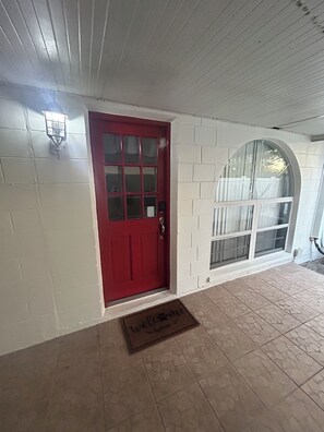 Une porte rouge avec une fenêtre, des murs recouverts de carreaux blancs et un sol carrelé.