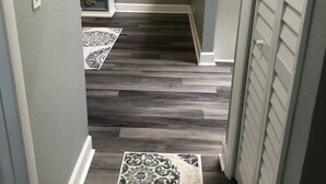 Un pasillo estrecho con suelo de madera oscura, un tapete estampado y una pequeña cocina con encimera y armarios blancos.