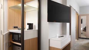 Une chambre d’hôtel moderne dotée d’une kitchenette, d’un téléviseur à écran plat fixé au mur et d’un plancher en bois.