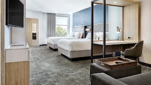 Une chambre d’hôtel avec deux lits, un bureau, une chaise, une télévision et un grand miroir.