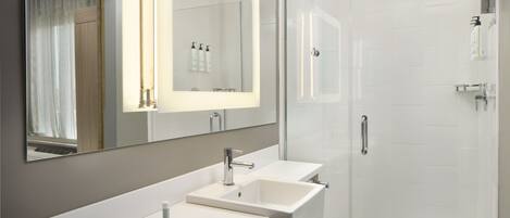 A modern bathroom with a large mirror, two sinks, a shower, and a toilet.