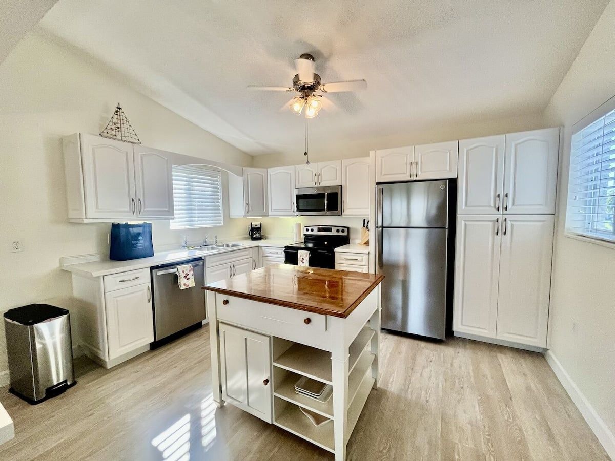 A kitchen with white cabinets, a stainless steel refrigerator, a microwave, and a wooden island.