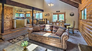 Ein gemütliches Blockhaus-Interieur mit einer großen Couch aus Holz, einem Essbereich und einer durch eine offene Tür einsehbarer Küche.