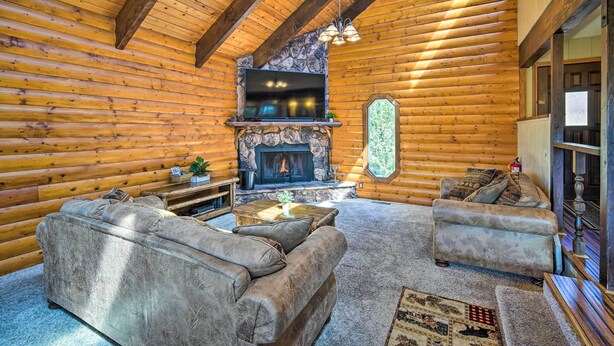 Ein rustikales Blockhaus-Interieur mit Kamin aus Stein, zwei Sofas, einem Couchtisch und einem Fernseher, der über dem Kamin angebracht ist.