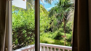A view from a balcony with a white railing, overlooking a lush garden with various plants and a palm tree. - Groundfloor "Pat's Place" @ Sapphire Beach Resort (San Pedro)