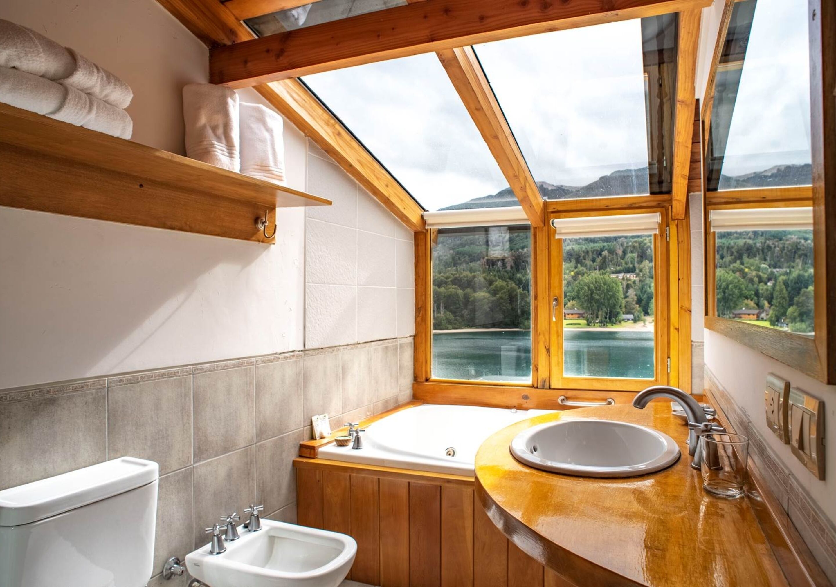A bathroom with a wooden vanity, a bathtub, a sink, and a window offering a view of a lake and mountains.