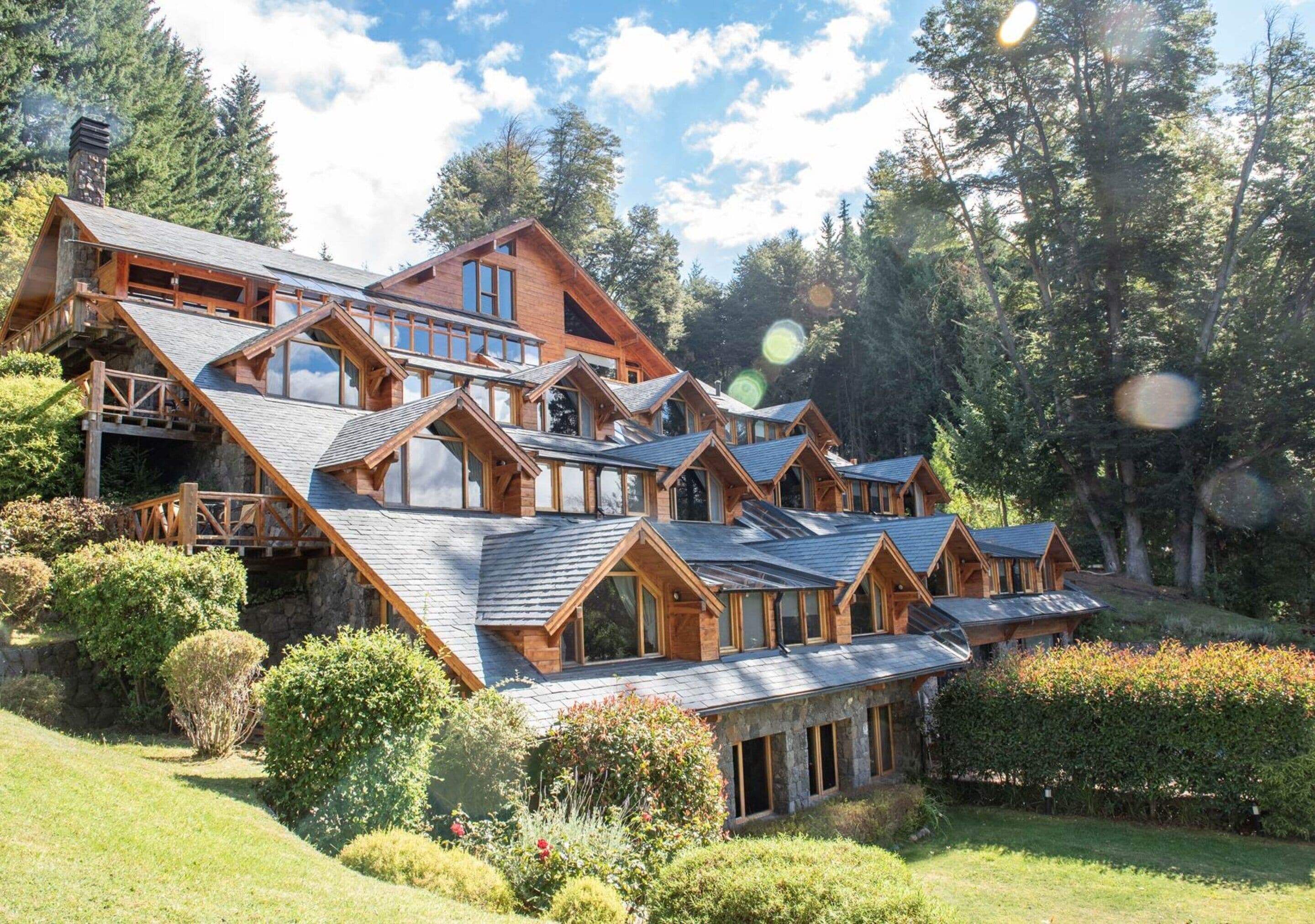 A large, multi-story lodge with a steeply sloped roof, wooden balconies, and a lush garden setting.