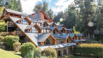 Un gran edificio tipo lodge de varios pisos con techo pronunciado, balcones de madera y un exuberante jardín.