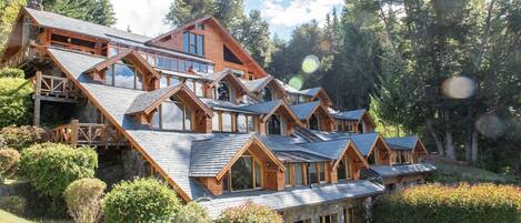 A large, multi-story lodge with a steeply sloped roof, wooden balconies, and a lush garden setting.