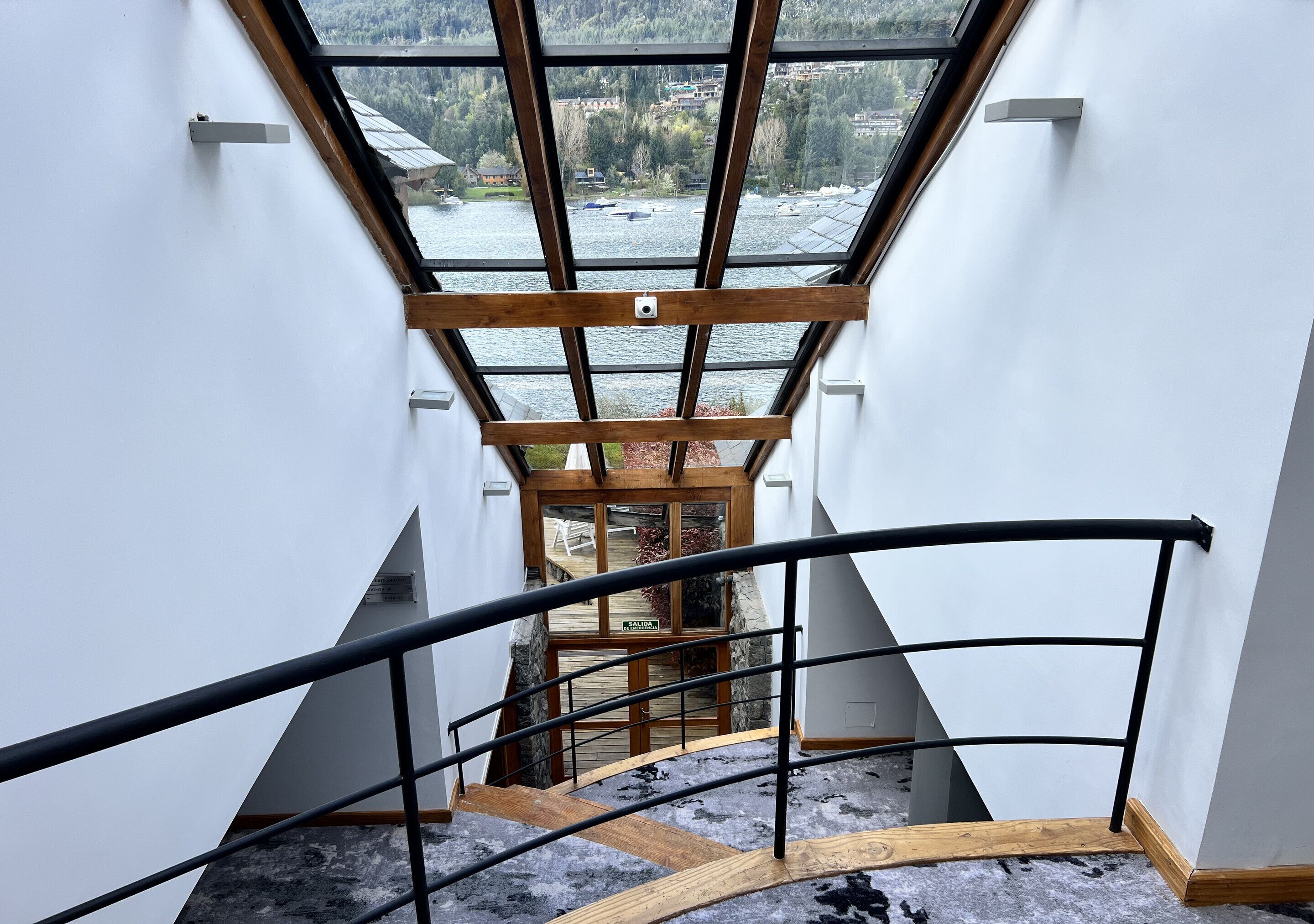 Vista desde un piso elevado con tragaluz, que conduce a una escalera de madera y una puerta de cristal con la leyenda 'SALIDA'.