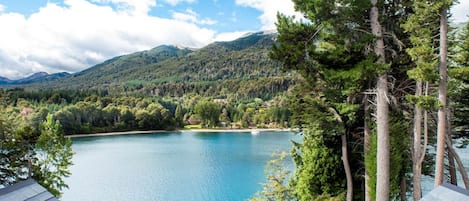 Vista sobre un lago con montañas al fondo, cielo despejado y un edificio de techo inclinado.
