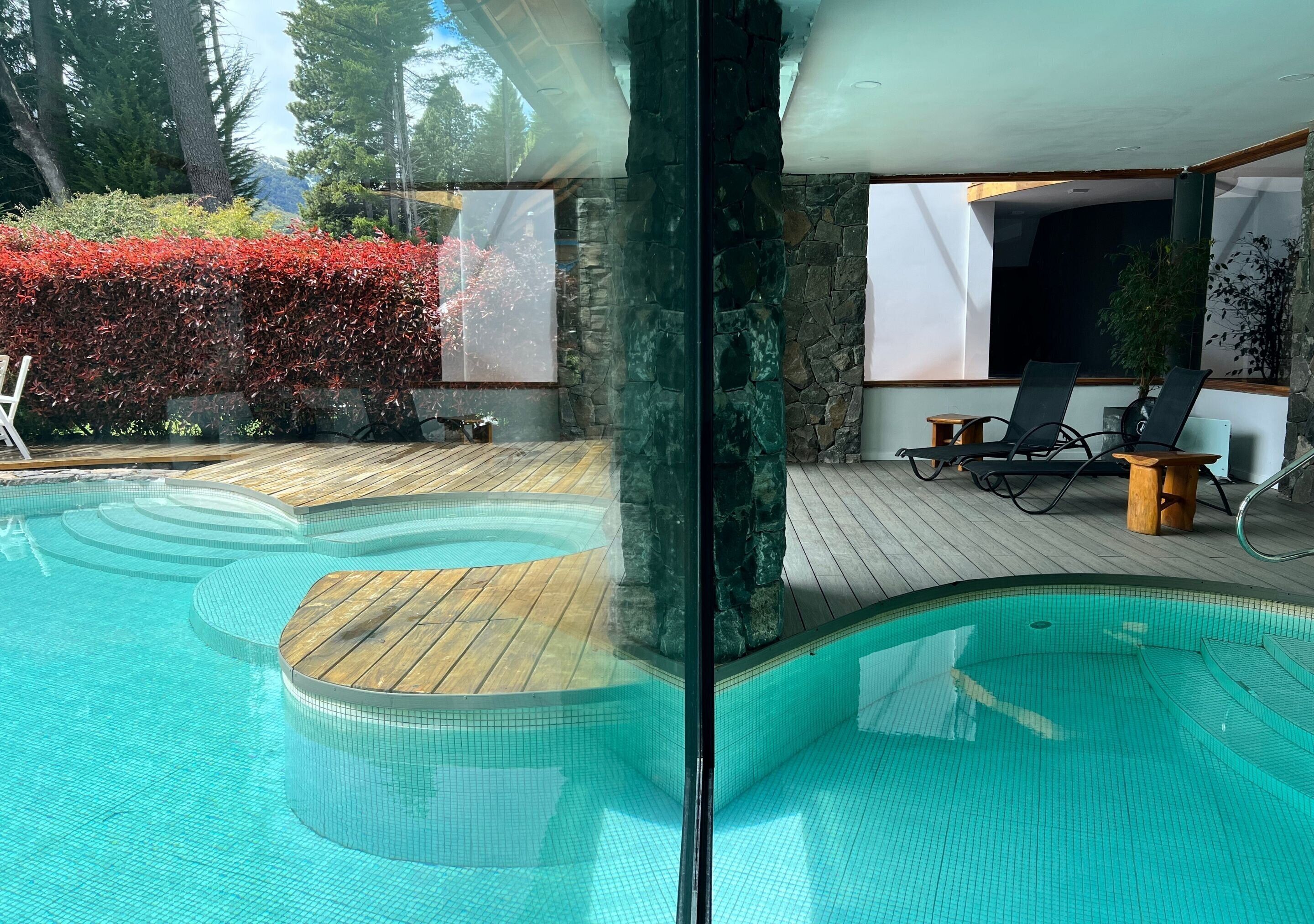 En swimmingpool med træterrasse, stenvægge og udendørs siddepladser.